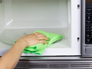 A person cleaning a microwave interior with a green cloth to prevent issues like the microwave not heating.