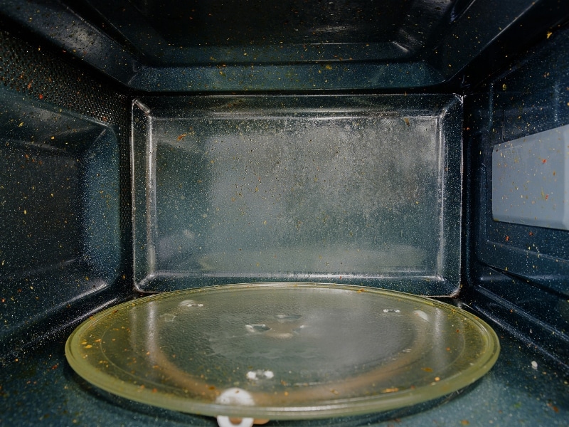 A dirty, rusty microwave with a turntable and splattered food debris.