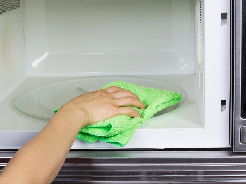 A close-up of a person cleaning a rusty microwave.