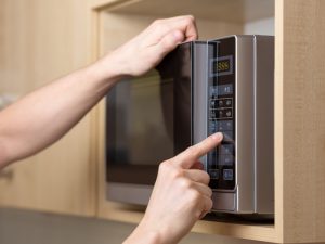 A hand presses the buttons on a microwave oven's control panel. The buttons appear unresponsive. The microwave may have a faulty keypad.