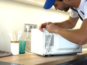 A person repairing a microwave at home due to microwave buttons not working, restoring its functionality.