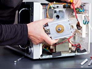 A technician checking a microwave oven, holding a microwave components part.