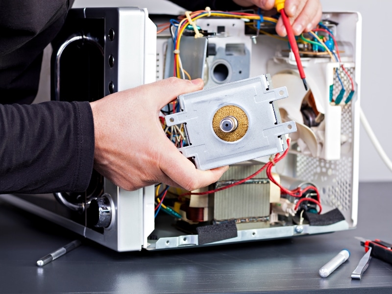 A close-up of a person repairing an old microwave, showing its internal components and wiring.