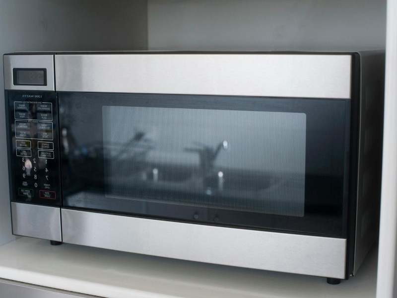 An energy efficient refurbished microwave oven with a stainless steel finish, sitting on a white countertop.