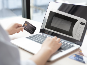 Person holding a credit card while shopping online for a microwave on a laptop, representing the process of buying a used microwave safely through e-commerce platforms.