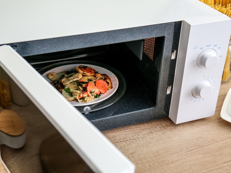 Plate of vegetables inside an older microwave, raising questions about signs of a faulty microwave.